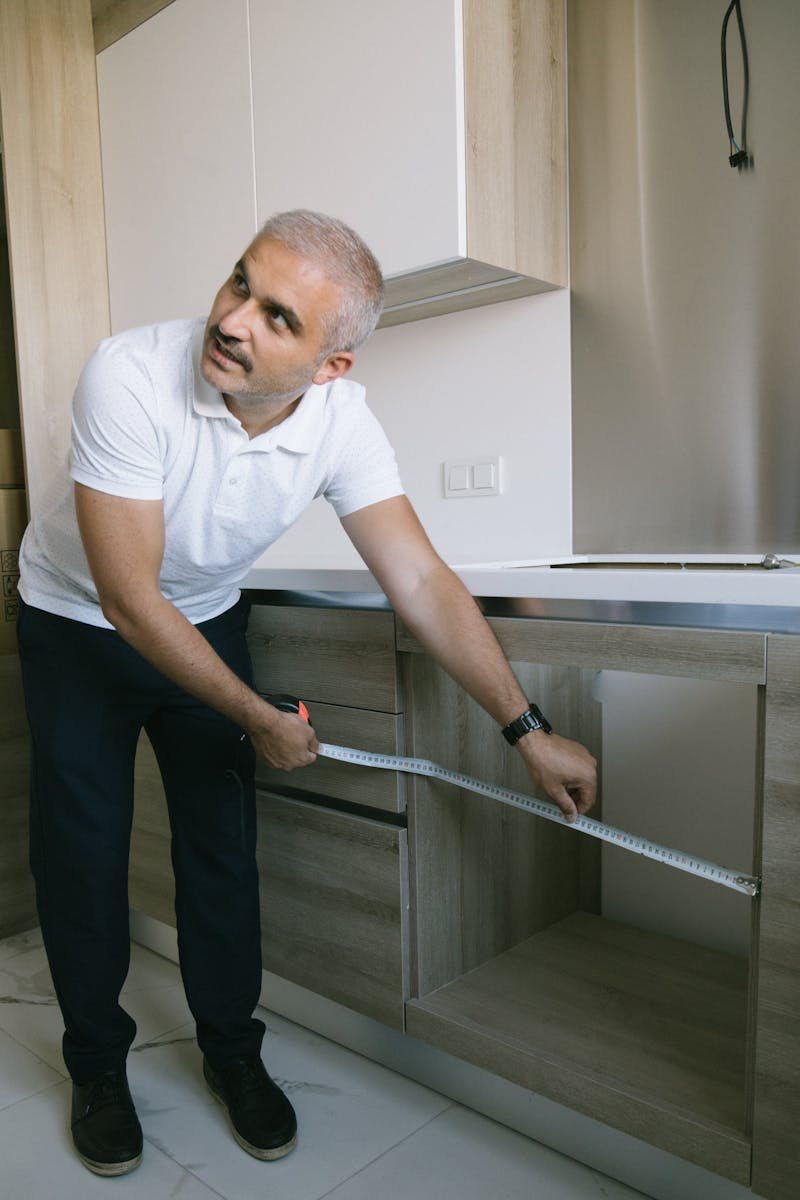 A man using a measuring tape to measure kitchen cabinets in a modern Istanbul apartment.